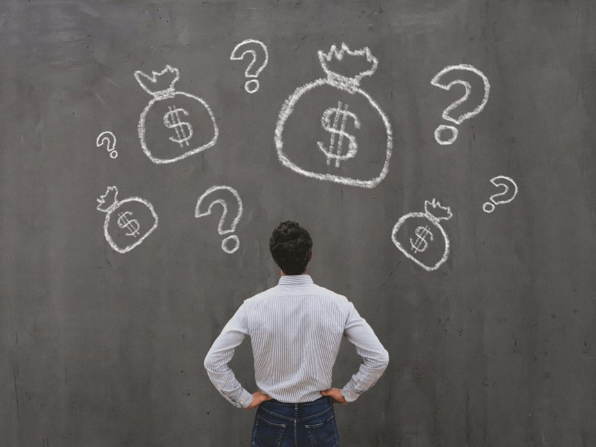 A man in a striped shirt stands facing a chalkboard with drawings of money bags and question marks on it.
